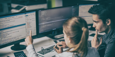 Two individuals analyzing data on multiple computers - Speed Reading for Business Professionals