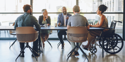 Diverse workplace team, including men, women, and people with disabilities, meeting to discuss strategy and goals.