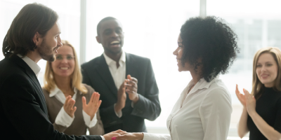 Grateful boss handshaking promoting african businesswoman congratulating with career achievement while colleagues applauding cheering successful worker, appreciation handshake, employee recognition