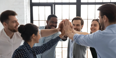 Group of employees high-fiving in the workplace - Building and Maintaining Team Synergy - Leading Change Initiatives