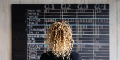 Rear view of a business woman looking at the project management calendar in her office - business concepts - Strategic Thinking and Decision Making Series - Achieving Maximum Productivity