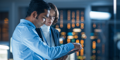 Technical professional leader consulting with a female manager and male colleague over a tablet, discussing development and coding in a modern tech facility.